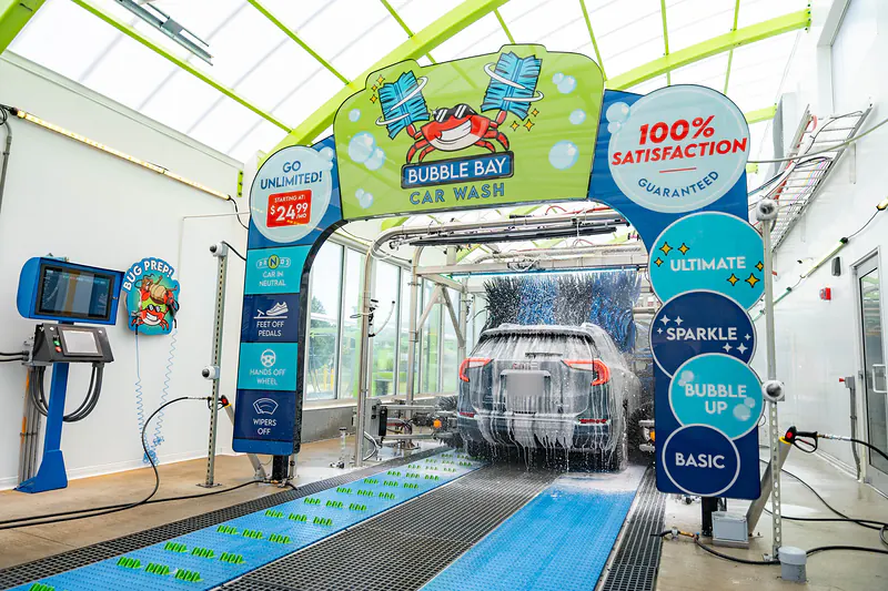 A foam-covered SUV in the wash tunnel, framed by the Bubble Bay crab arch and the four package signs