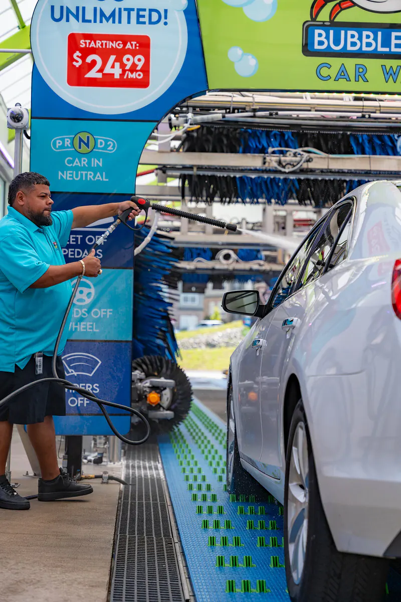 A team member in a teal Bubble Bay polo hand-prepping a white car at the tunnel entrance