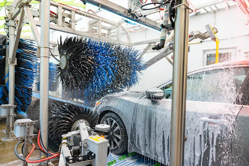 Blue and black brushes scrubbing a soapy sedan inside the wash tunnel