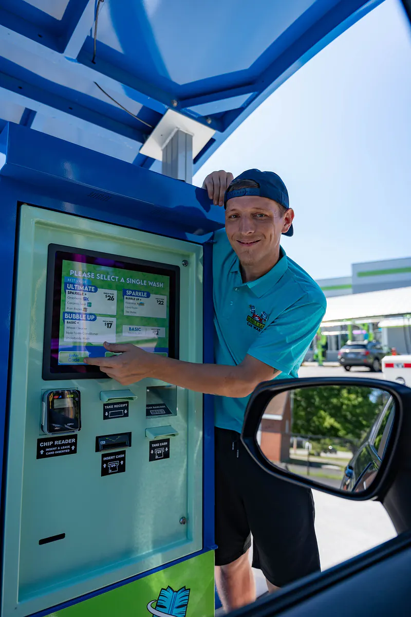 A smiling Bubble Bay team member tapping the pay kiosk screen, seen from the driver’s window